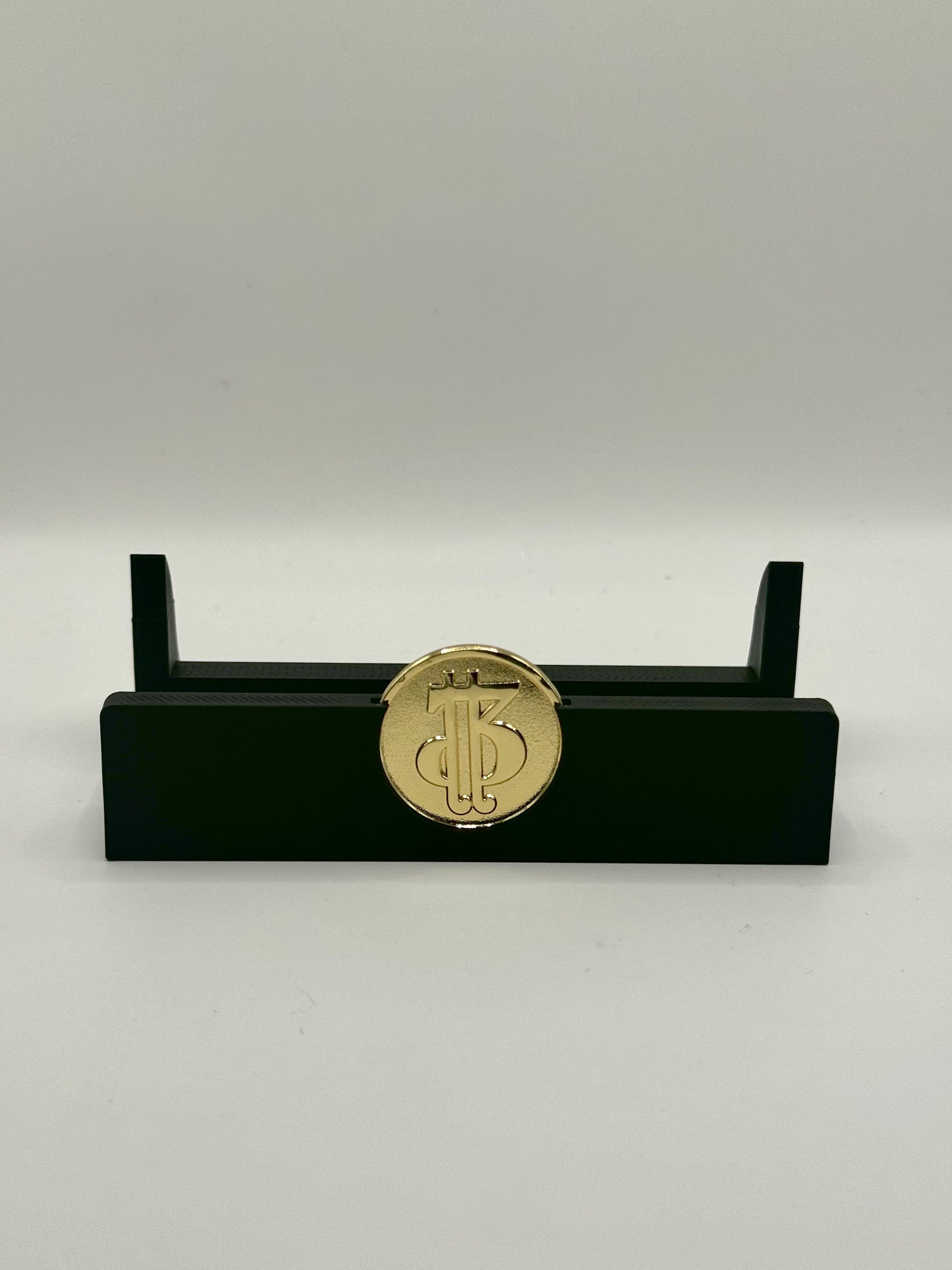 A black Piggybanx coin stand displaying a gold-colored coin with an artistic design.